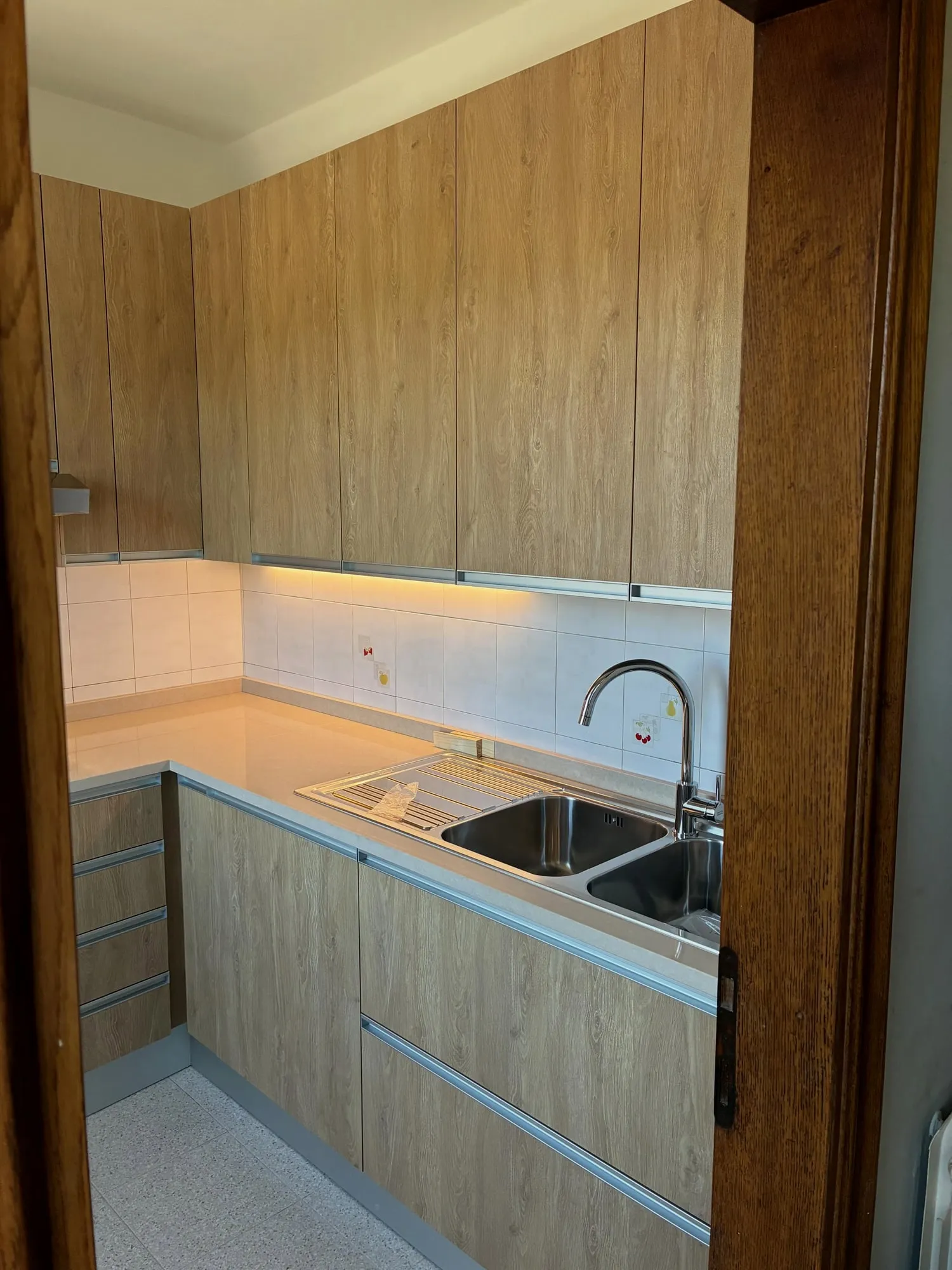 La stessa cucina finita: ante effetto legno, piano in quarzo e illuminazione sotto i pensili