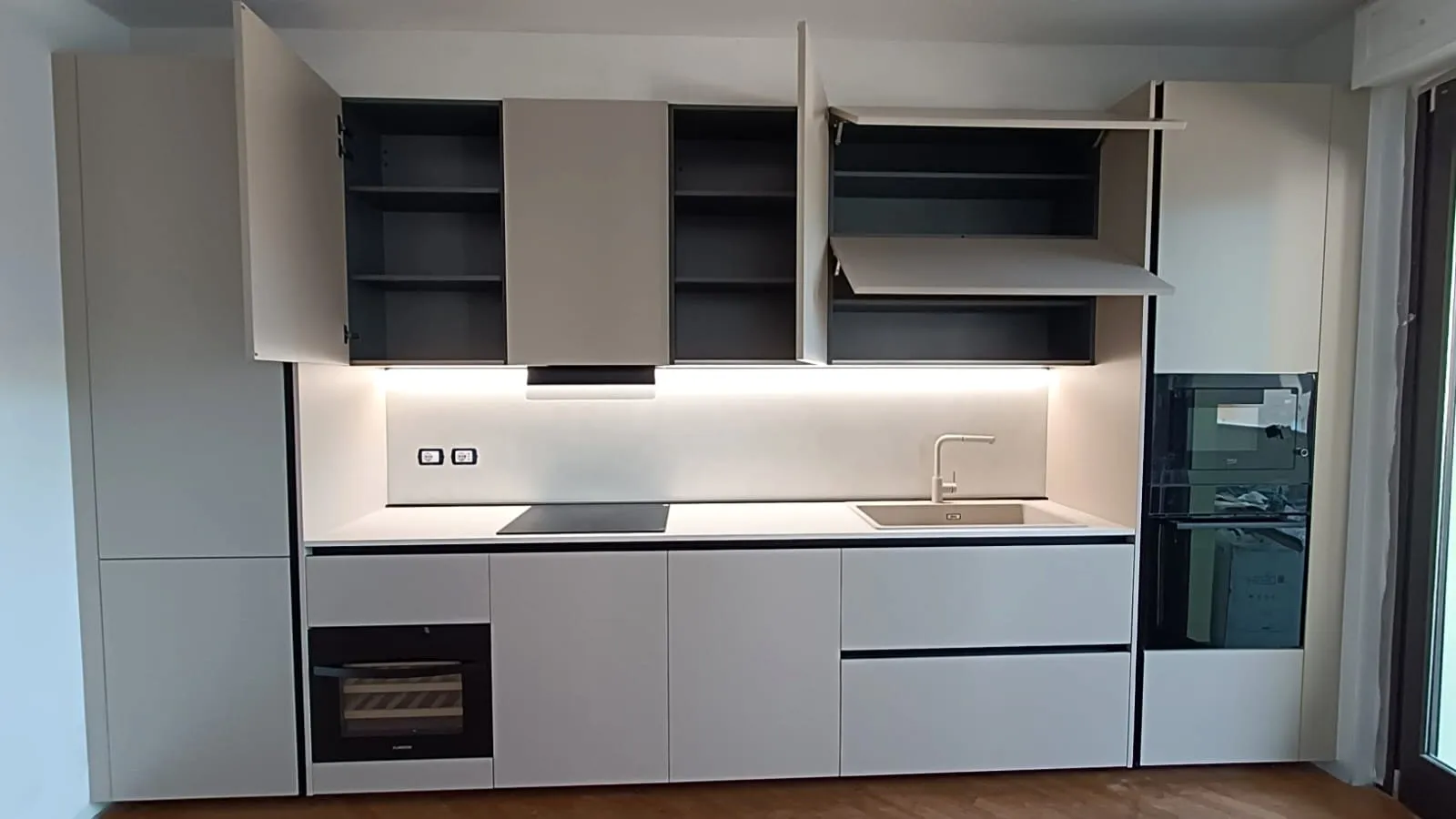 La stessa parete a lavoro finito: cucina lineare con gole nere, forno a colonna e illuminazione integrata