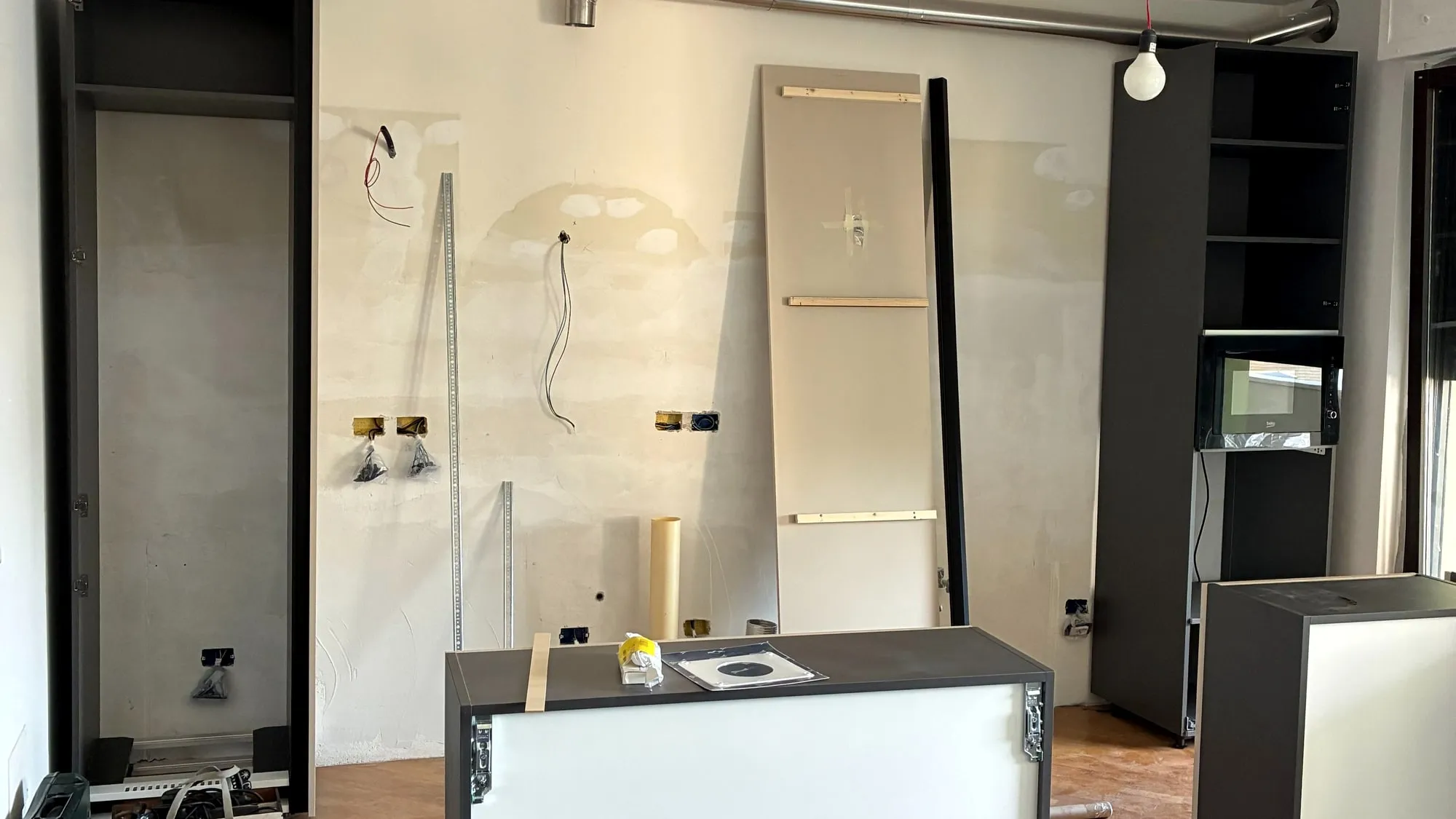 La parete della cucina in cantiere, con gli impianti a vista e i pannelli appoggiati