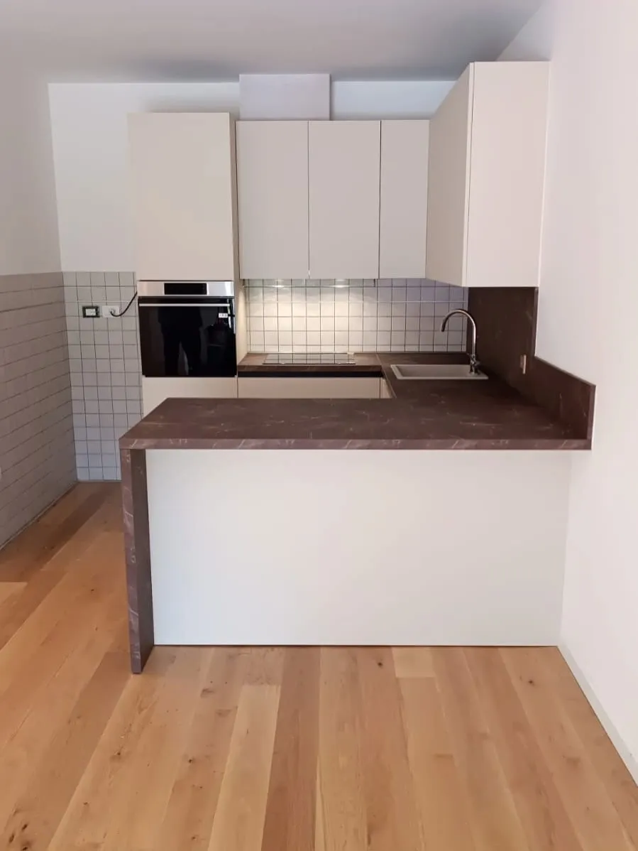 La stessa stanza con la cucina bianca montata e la penisola con il piano in pietra
